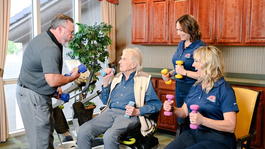 A senior man doing light strength exercises with support from his care team